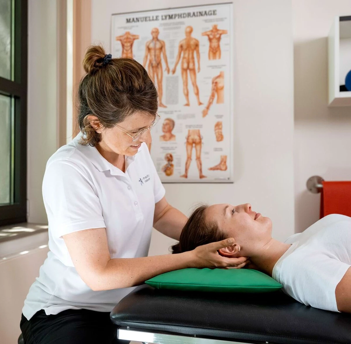 Individuelle physiotherapeutische Behandlung – eine Therapeutin arbeitet gezielt an der Schulter einer liegenden Patientin im medicos.Osnabrück.
