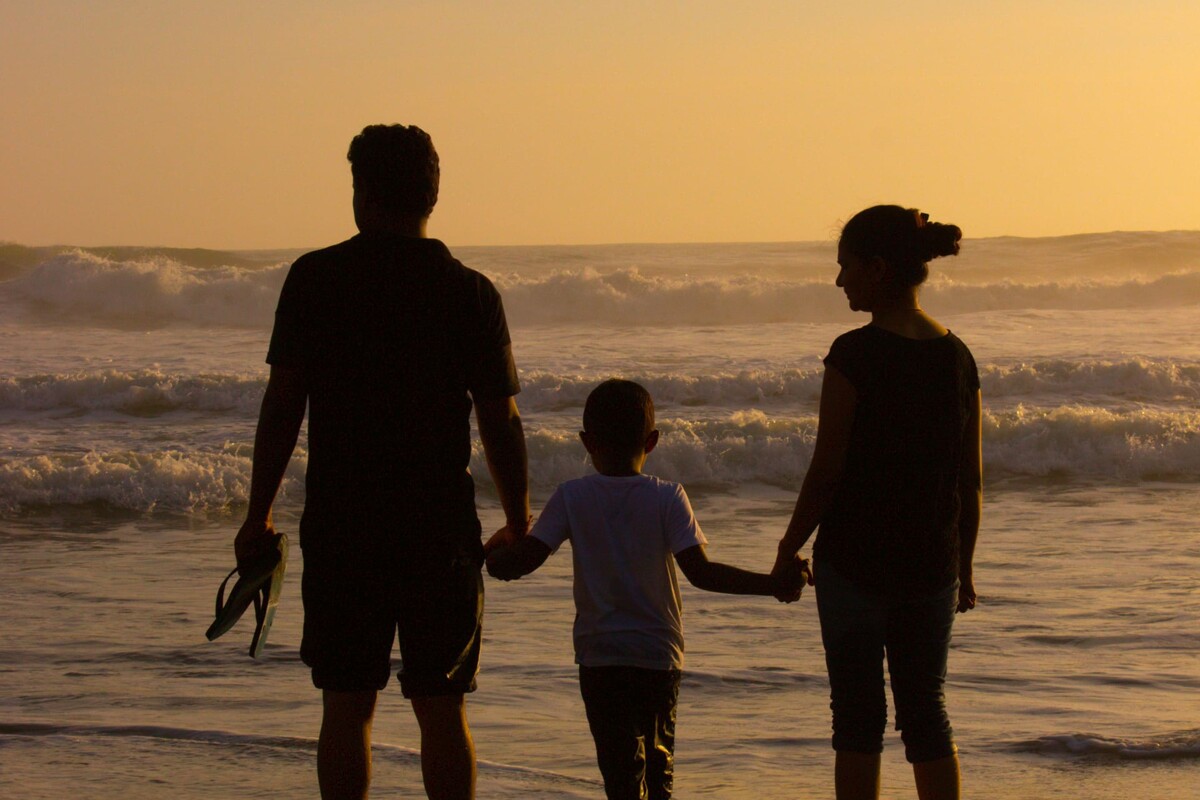 Silhouette einer dreiköpfigen Familie, die im Sonnenuntergang am Strand steht und sich an den Händen hält